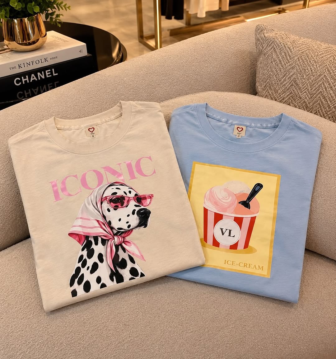 Duas T-shirts com estampas diferentes, uma clara e outra azul, sobre um sofá